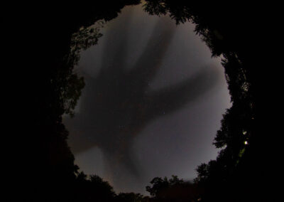 Shadowy hand silhouette seen through a dark, circular opening.