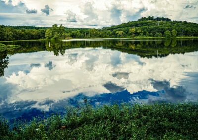 Calm lake reflecting clouds and green hills under a blue sky.
