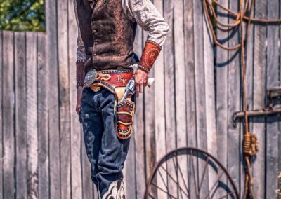 Man in stylish outfit stands against rustic wooden fence with a wagon wheel.