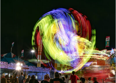 Colorful light trails create a vibrant swirl at a night carnival.
