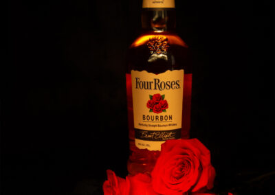 A bottle of Fire House whiskey illuminated against a dark background with red roses.