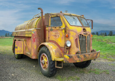 Rusty old tanker truck parked on gravel under blue sky.