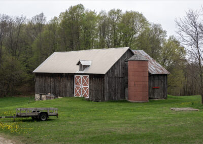Rustic wooden barn with a red silo in a green field.