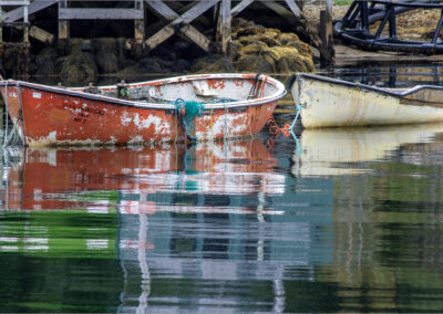 Two old boats floating side by side on calm water near a dock.