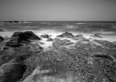 Black and white image of rocky shoreline with waves crashing.