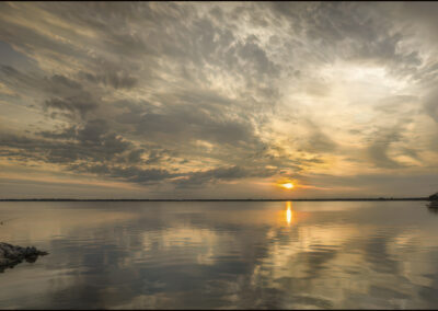 Sunset reflecting on a calm lake under a cloudy sky.