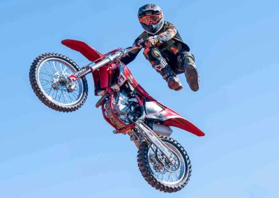 A motocross rider performing a mid-air stunt on a red dirt bike.