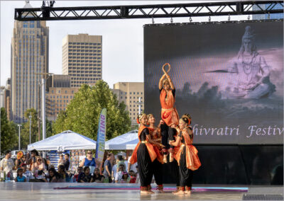 Traditional dance performance on outdoor stage with city backdrop.