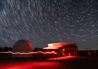 Star trails swirl above an illuminated observatory at night.