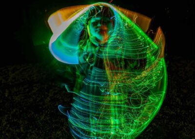 Person creating vibrant green and blue light trails in the dark.