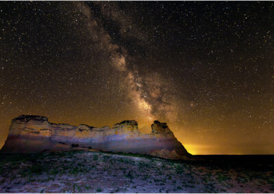 A starry night sky with the Milky Way glowing above rocky terrain.