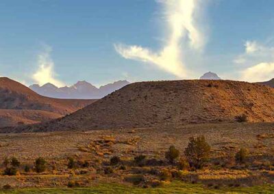 A scenic desert landscape with a hill and mountains under a blue sky.