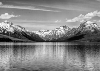Black and white landscape of snowy mountains reflected in a calm lake.