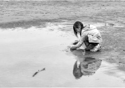 A child crouches by the water's edge, playing with the sand and waves.