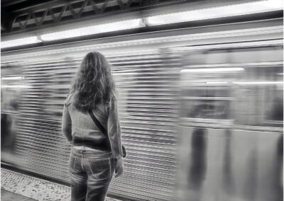 A woman waits on a subway platform as a train rushes by.