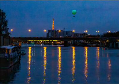 City skyline at dusk with a hot air balloon and reflected lights on water.