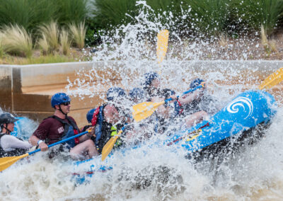 Group white-water rafting through rough rapids with splashing water.