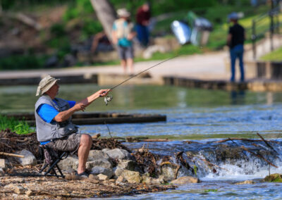 A young boy fishing by the rocky shore with a focused expression.