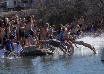Group of people jumping into a lake on a sunny day.