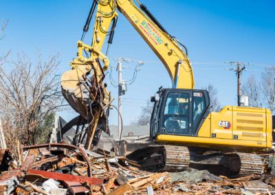 Yellow excavator clearing scrap metal at a demolition site.