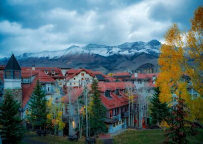 Autumn village with red roofs under snowy mountains and cloudy sky.