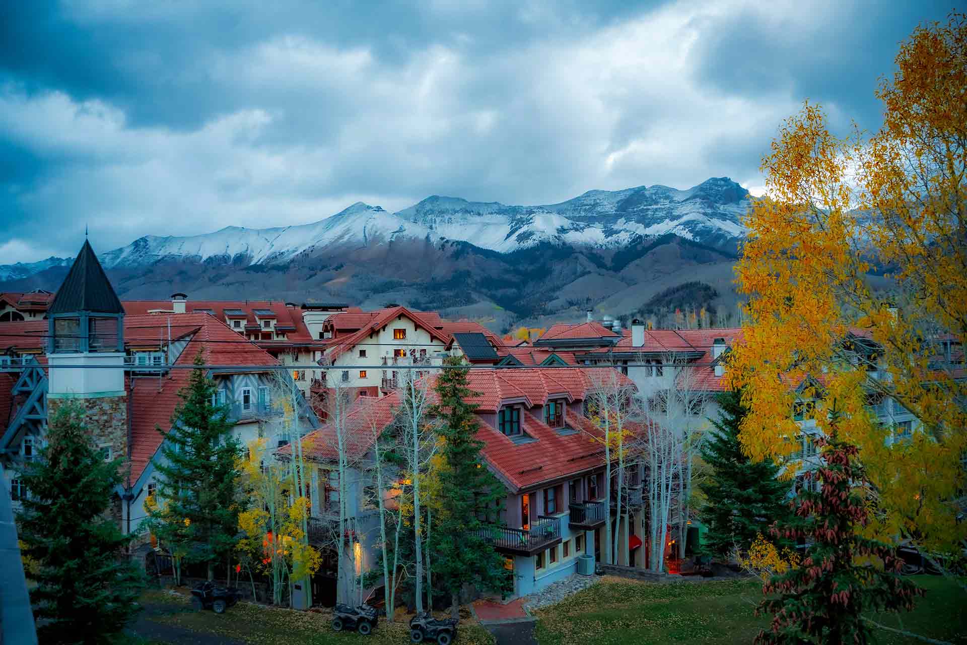 Autumn village with red roofs under snowy mountains and cloudy sky.