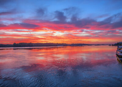Vibrant sunset over calm water with colorful clouds reflecting on the surface.