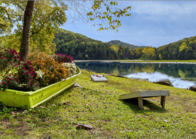 Lakeside garden with flowers, cornhole boards, and mountain views under a clear sky.