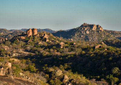 Scenic landscape of rocky hills with sparse vegetation under a clear sky.
