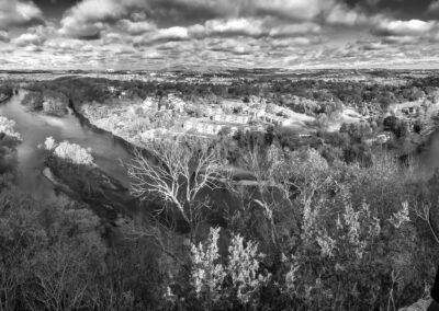 Black and white aerial view of a river winding through a town surrounded by trees.