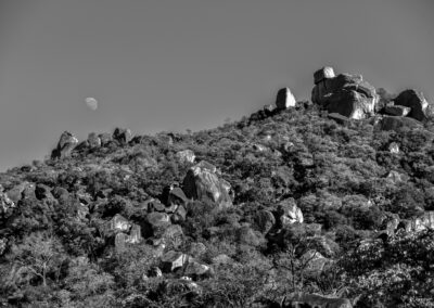Black and white photo of a rocky hill with the moon visible in the sky.