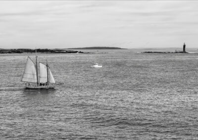 A sailboat and a motorboat on a calm sea with distant land under a cloudy sky.