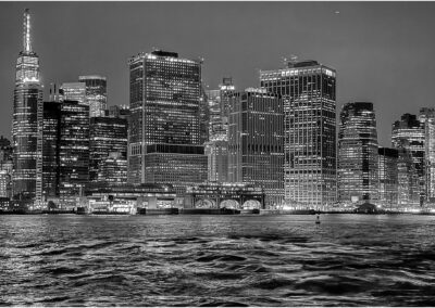 Black and white city skyline at night with illuminated buildings by the water.