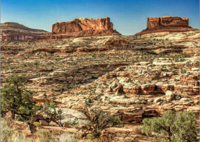 Rocky desert landscape with red cliffs under a clear blue sky.
