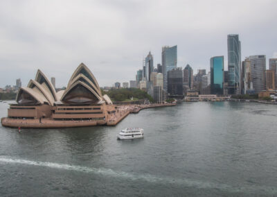 Sydney Opera House with city skyline and ferry on the water.
