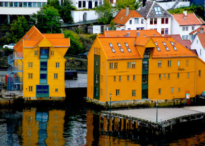 Bright yellow buildings with orange roofs reflect on calm waterfront in a quaint town.