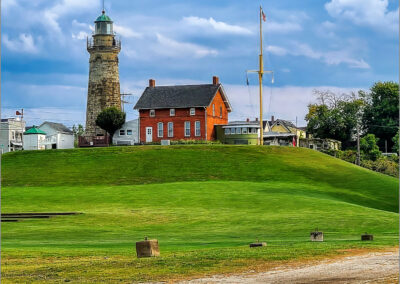 Historic lighthouse and red brick building atop a green hill under a cloudy sky.