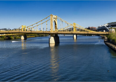 Yellow suspension bridge over a calm river under clear blue sky.