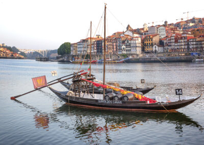 Traditional wooden boats docked on a calm river with a historic cityscape in the background.