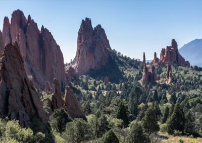 Red rock formations towering over a forested valley under a clear blue sky.