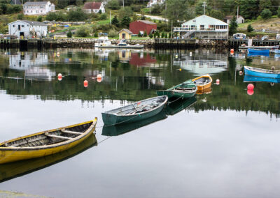 Colorful small boats floating on calm water with village reflections.