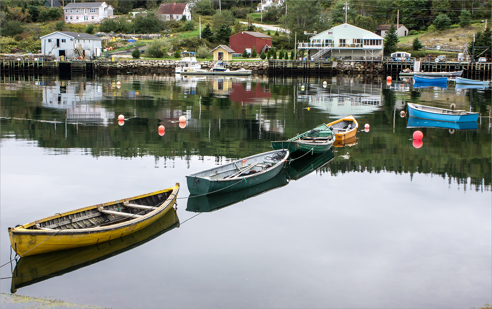 Colorful small boats floating on calm water with village reflections.