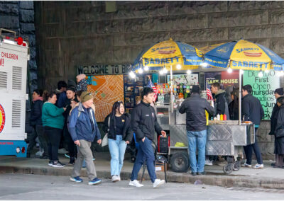 People waiting in line at a Sabrett hot dog stand on a city street at night.