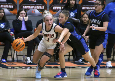 Female basketball player in white dribbling past a defender in blue during a game.