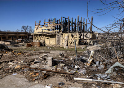 Partially destroyed building with debris scattered around under a clear blue sky.