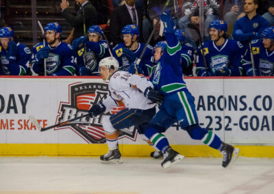 Two ice hockey players compete intensely near the boards during a game.