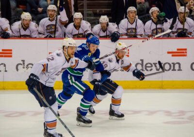 Two Anaheim Ducks players defend against a Vancouver Canucks player on the ice.