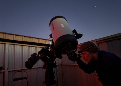 Person observing the night sky through a large telescope at dusk.