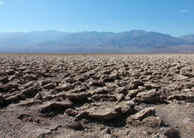 Cracked desert ground with mountains in the background under a clear sky.