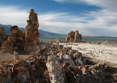 Rock formations and tufa towers near a lake under a partly cloudy sky.